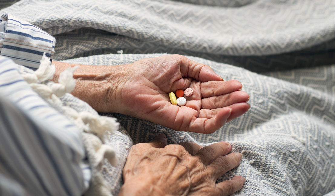 Elderly hands holding various pills
