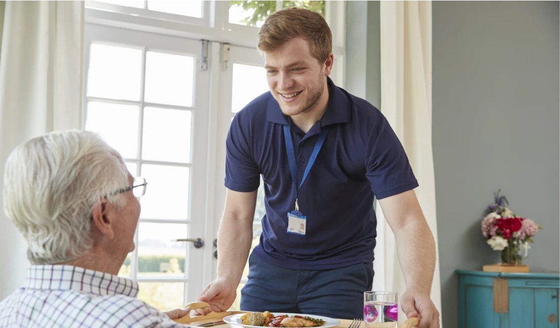 Caregiver serving meal to elderly man